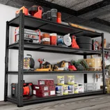 A garage shelf holds various tools and supplies, including power tools, extension cords, tires, paint cans, and boxes.