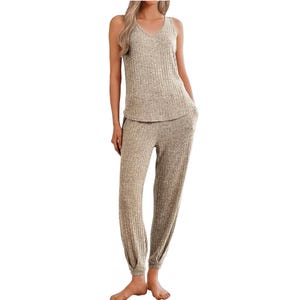 A women's two-piece pajama set featuring a ribbed, sleeveless V-neck top and matching loose-fit pants in a light beige color. The set has a cozy, textured fabric with a relaxed fit.