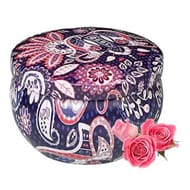 Decorative round ottoman with paisley pattern in blue and pink tones accompanied by two pink roses.