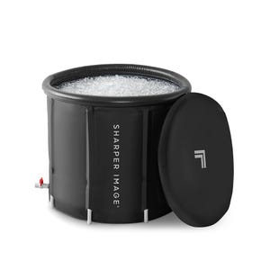The Sharper Image Cold Plunge Ice Bath is a black, cylindrical ice bath with \“SHARPER IMAGE\“ branding on the side, featuring an accompanying lid. Designed for cold-water immersion, it includes a drain valve at the bottom.