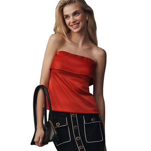 A woman wears a strapless red top and a black skirt with white-trimmed pockets, holding a black handbag.