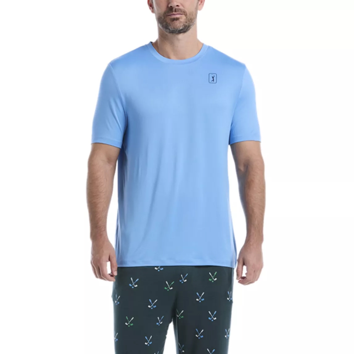 A man is wearing a light blue short-sleeve T-shirt with a small logo on the chest and dark pants featuring green and blue crossed designs.