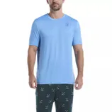 A man is wearing a light blue short-sleeve T-shirt with a small logo on the chest and dark pants featuring green and blue crossed designs.