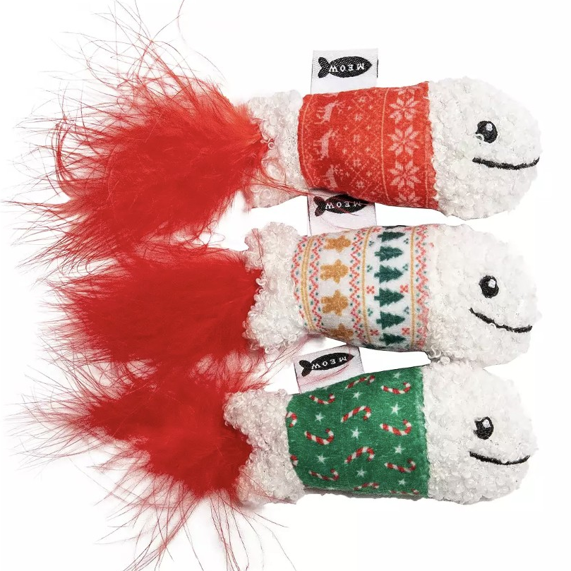 Set of three plush cat toys with white fluffy bodies, festive red and green patterned covers, and red feather tails. Each toy features a different holiday design with a \“Meow\“ tag.