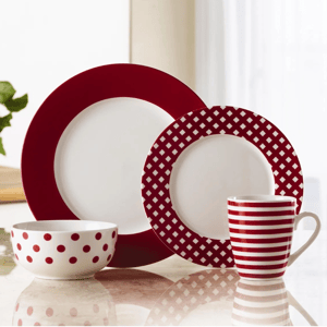 A dishware set with red and white patterns featuring a large plate with a solid red rim, a smaller plate with a red lattice design, a bowl with red polka dots, and a mug with red horizontal stripes.