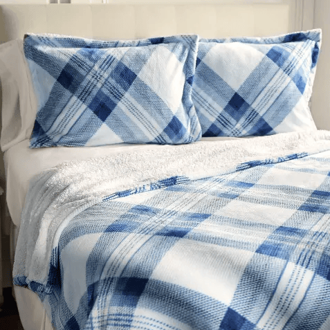 A bed is neatly made with blue and white plaid patterned pillows and matching blanket, complemented by a white sheet underneath.