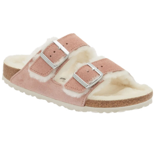 A pink suede slide sandal with two silver buckles and a white shearling lining, featuring a cork footbed and a textured rubber sole.
