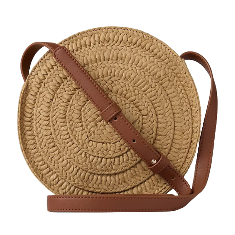 Round straw crossbody bag with a braided design, tan leather strap, and adjustable buckle.