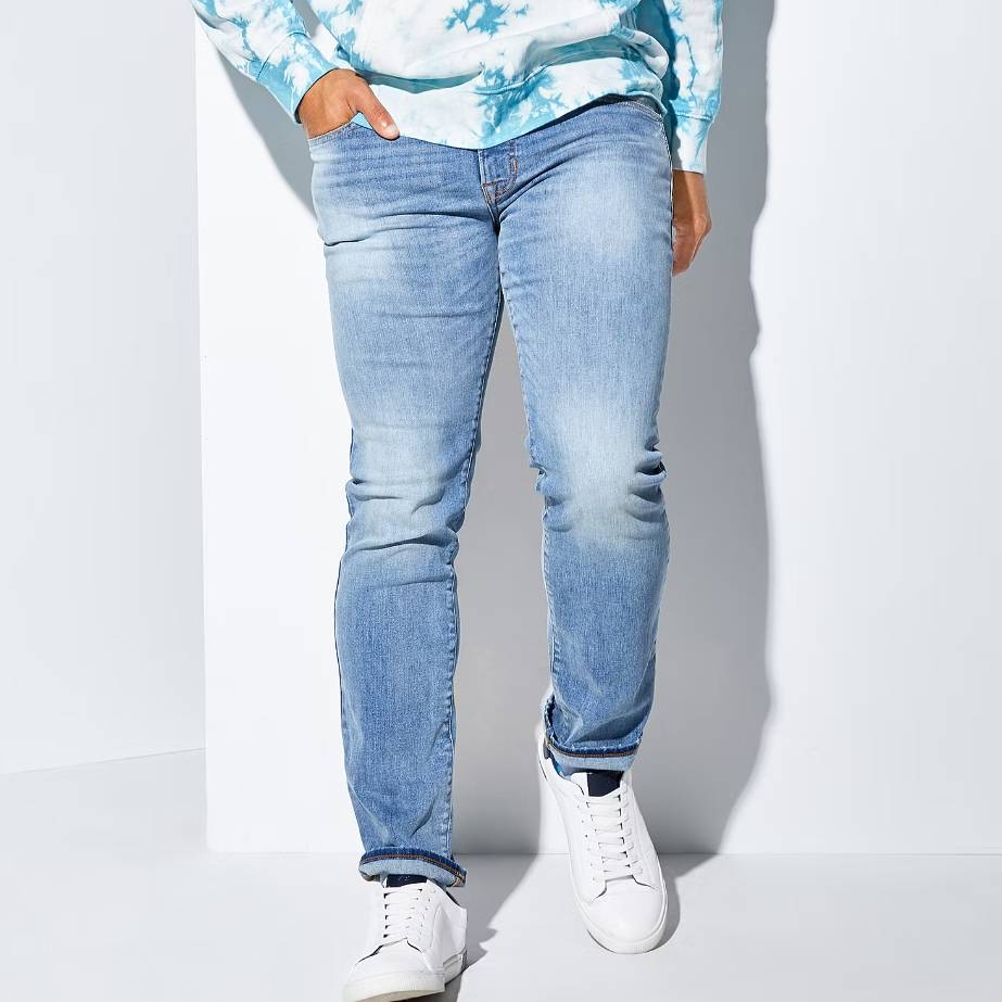 A person wearing light blue faded jeans and white sneakers.