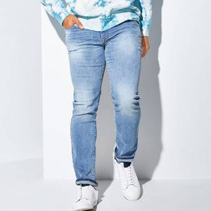A person wearing light blue faded jeans and white sneakers.