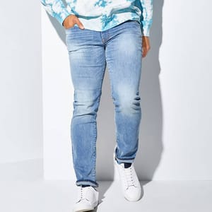 A person wearing light blue faded jeans and white sneakers.
