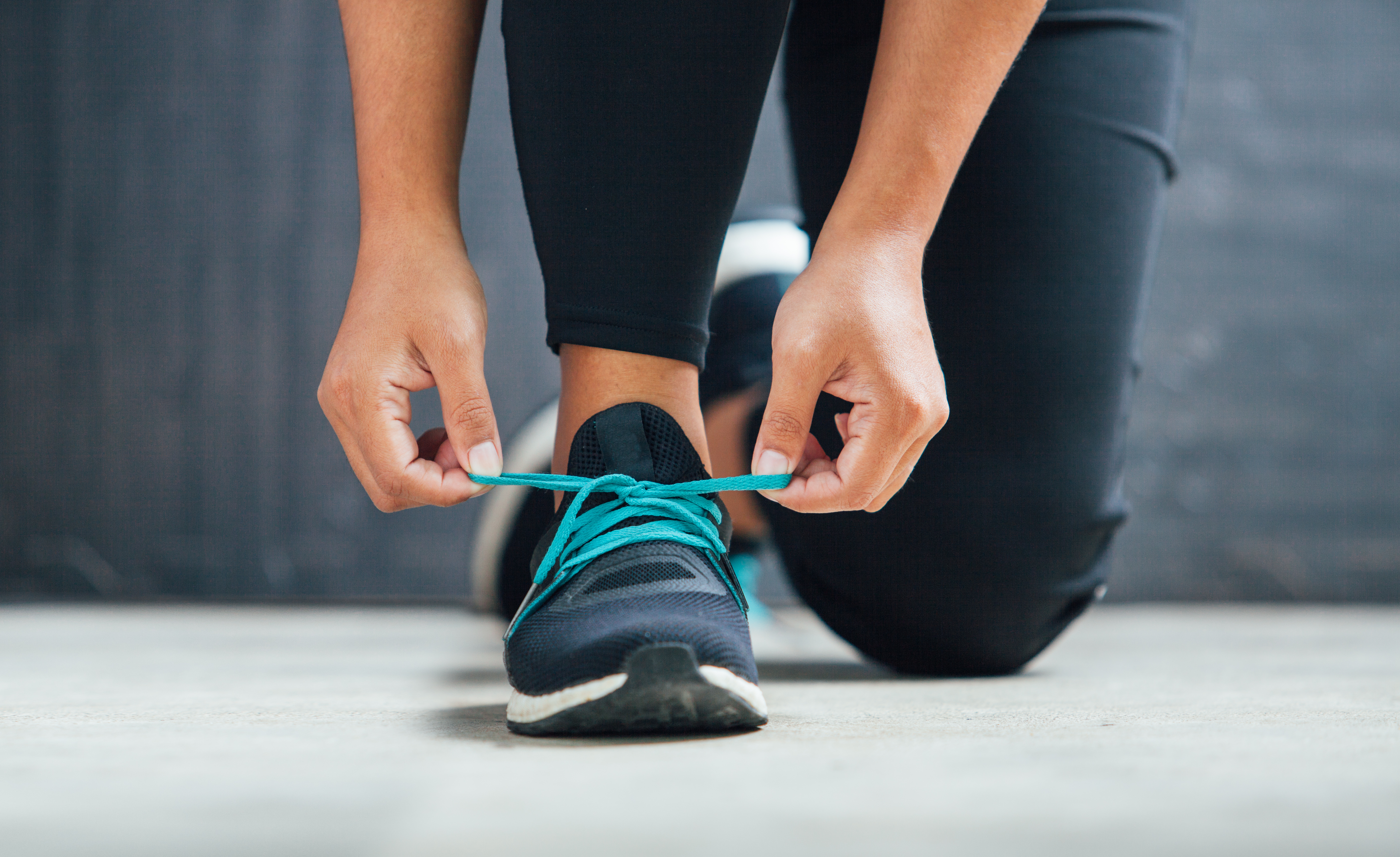 A person is tying the laces of a black athletic shoe with bright blue laces.
