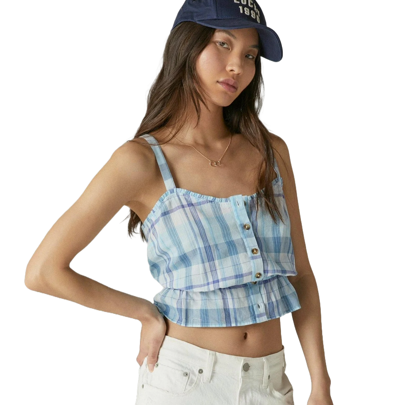 A woman is wearing a blue plaid crop top with buttons and white pants, paired with a navy baseball cap.