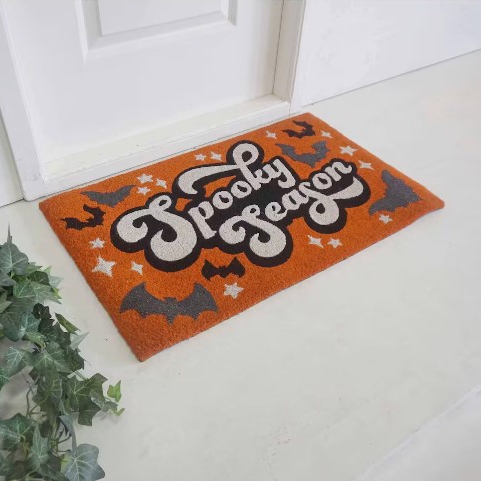 An orange doormat with the words \“Spooky Season\“ surrounded by black bats and white stars, suggesting a Halloween theme.
