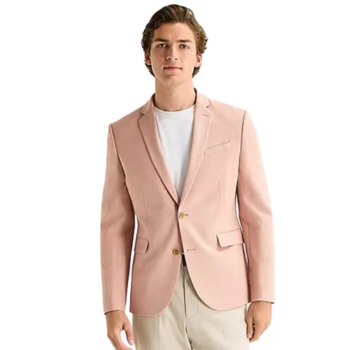 A man is wearing a light pink blazer over a white t-shirt, paired with beige pants. The blazer features a notch lapel, two-button closure, and front pockets.