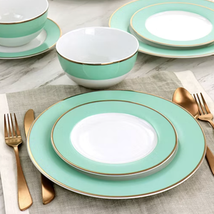 A dinnerware set with mint green and white plates, a bowl, and gold accents is arranged on a linen placemat, accompanied by gold-colored cutlery.