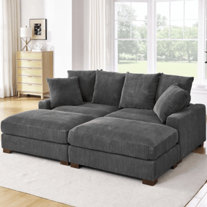 A gray corduroy sectional sofa with multiple cushions is placed on a light-colored rug in a bright, modern living room featuring large windows and wooden flooring. A light wood dresser and a potted plant are in the background.