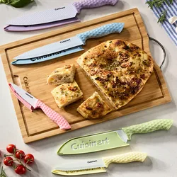 A wooden cutting board displays a sliced focaccia and a set of colorful Cuisinart knives with textured handles in pink, blue, yellow, green, and purple. Cherry tomatoes and rosemary are also visible.