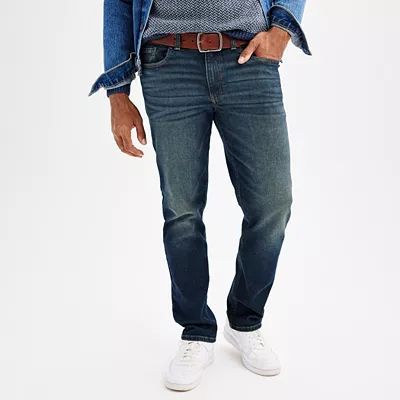A model wears a pair of mid-rise, straight-leg Sonoma Goods For Life jeans in a classic blue wash, complemented with a brown belt and white sneakers.