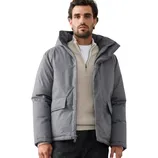 A man wearing a gray puffer jacket, cream textured sweater, black pants, and brown hiking boots.