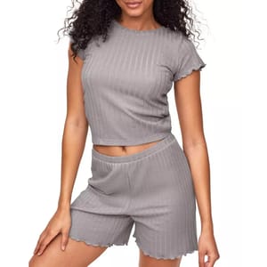 The Adore Me Lilliana set features a gray, ribbed T-shirt with short sleeves and a matching pair of shorts. Both pieces have a comfortable and relaxed fit with subtle ruffled edges for a casual look.