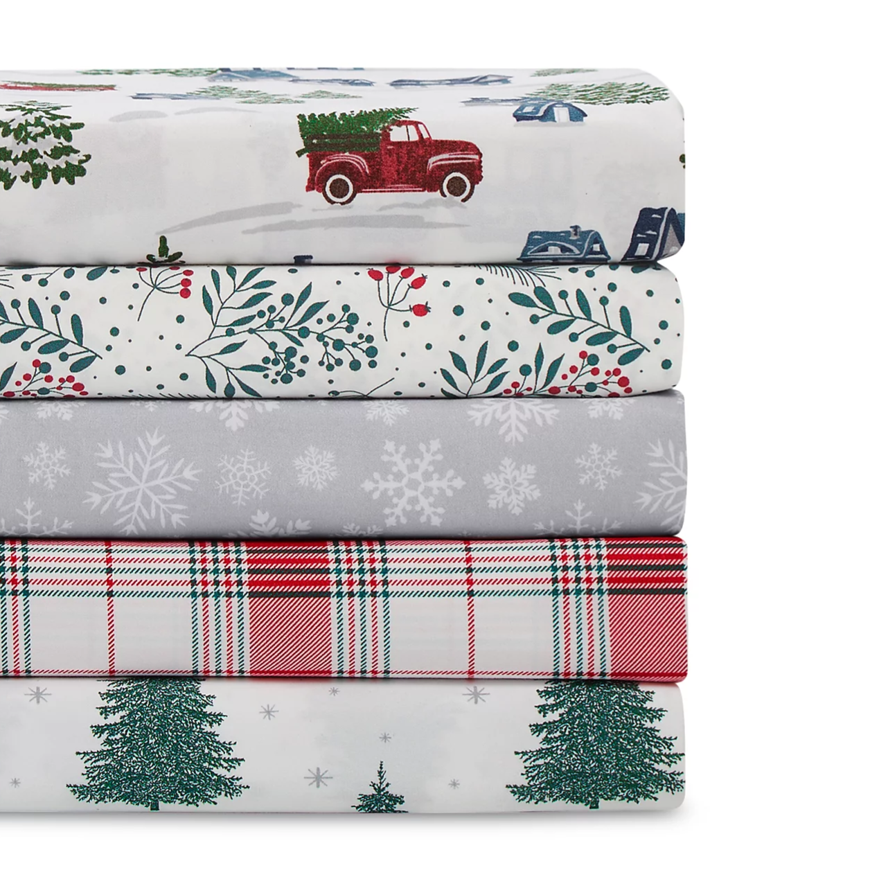 A stack of folded bedsheets with festive designs: a red truck with a Christmas tree, berry and foliage pattern, snowflakes on gray, red and green plaid, and green trees with snowflakes.