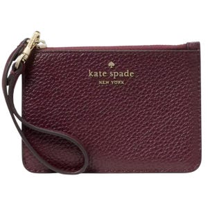 A small, textured leather wristlet in dark burgundy with \“kate spade NEW YORK\“ embossed in gold lettering. It features a wrist strap attached to a gold zipper pull.
