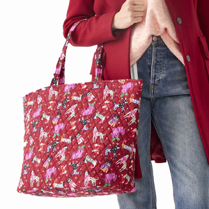 A person is holding a red quilted tote bag with colorful cupcake patterns.