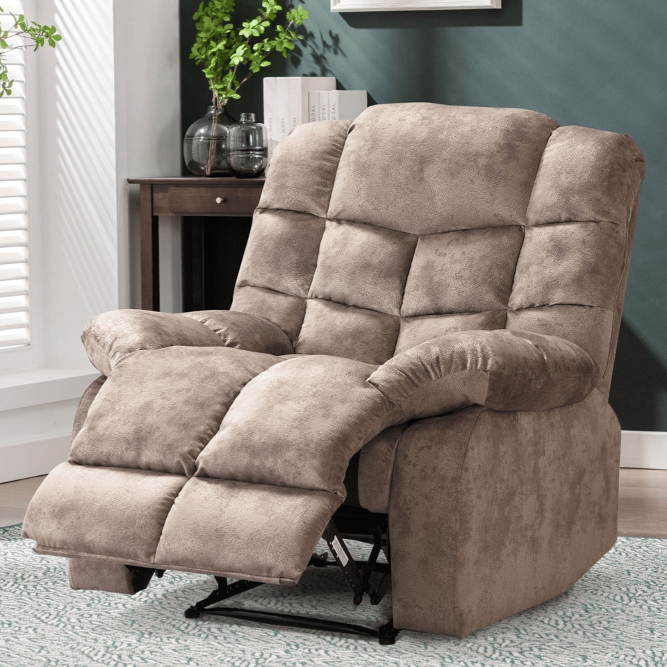 Plush beige recliner with cushioned armrests and an extended footrest, set in a cozy living room with a side table, plant, and framed artwork on a green wall.