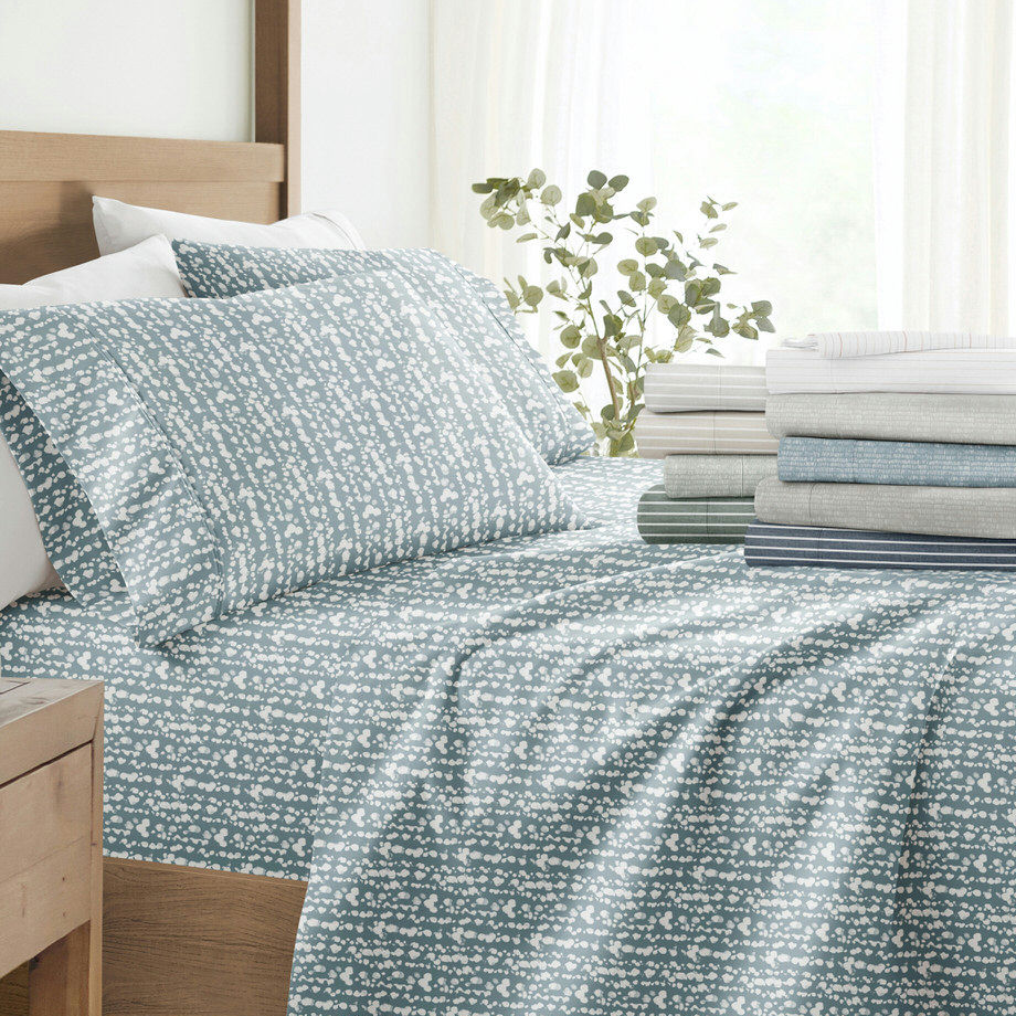 Bed with blue and white patterned bedding set, stacked sheets on side, and a potted plant.