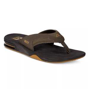 Reef sandals featuring a thong design with a bottle opener integrated into the rubber sole; they have brown fabric straps marked with \“Reef\“ and are set on a black footbed with contrast detail at the heel.