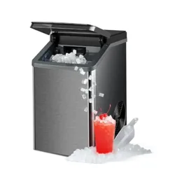 A countertop ice maker dispenses ice cubes next to a red drink garnished with cherries, accompanied by an ice scoop.