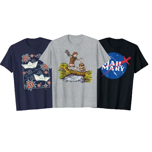Three graphic T-shirts are displayed: one with paper boats and flowers, one featuring a cartoon of a child and a tiger by a pond, and one with a parody logo saying \“Hail Mary.\“