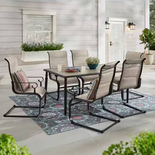 A patio furniture set with a table, four chairs, one rocking chair, and two patterned rugs.