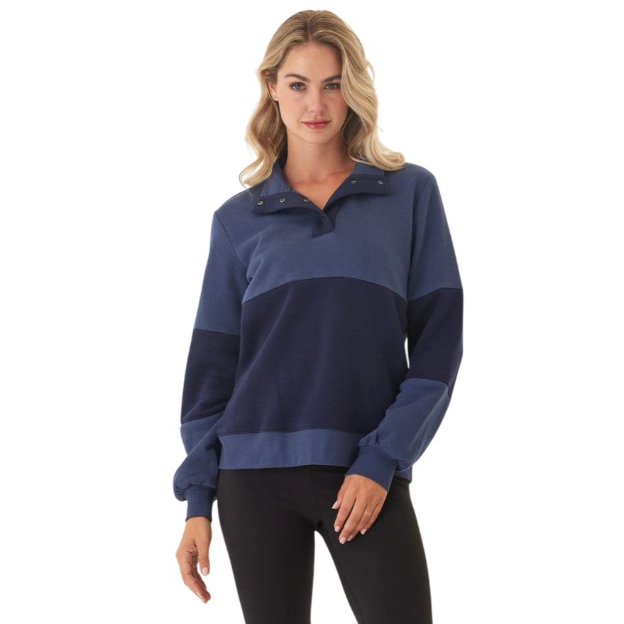 A woman is wearing a two-tone blue pullover with a buttoned collar and long sleeves, paired with black leggings.