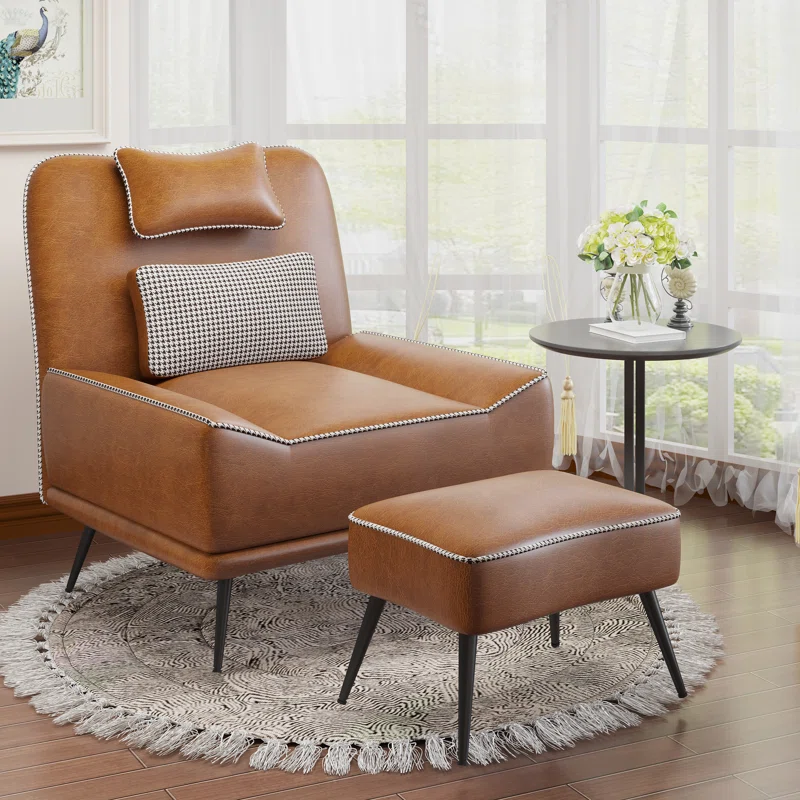 A brown upholstered side chair with a matching ottoman, featuring a houndstooth accent cushion and nailhead trim, sits on a fringed circular rug with a nearby small round table and floral arrangement.