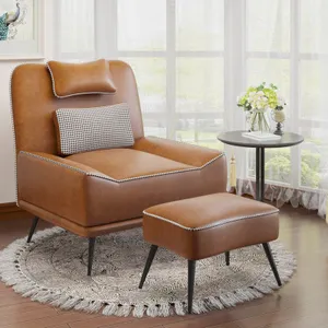 A brown upholstered side chair with a matching ottoman, featuring a houndstooth accent cushion and nailhead trim, sits on a fringed circular rug with a nearby small round table and floral arrangement.