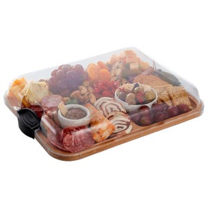 A charcuterie board with a clear cover featuring assorted cheeses, meats, nuts, grapes, crackers, stuffed olives, and spreads, all neatly arranged on a wooden base.