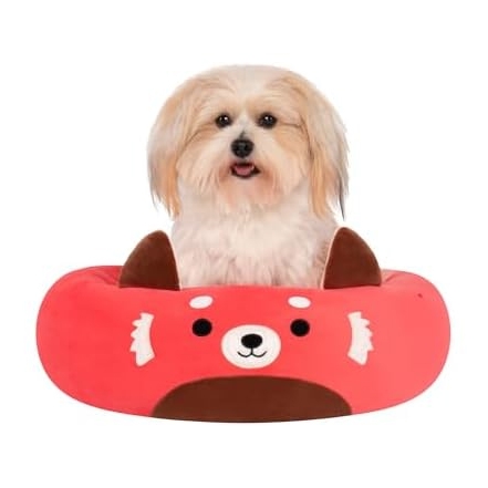 A small dog is sitting in a bright red, plush pet bed designed to look like a red panda, complete with ears and a cute face.