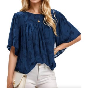 A blue blouse with textured fabric features bell sleeves and a loose silhouette, paired with white pants and a gold necklace.