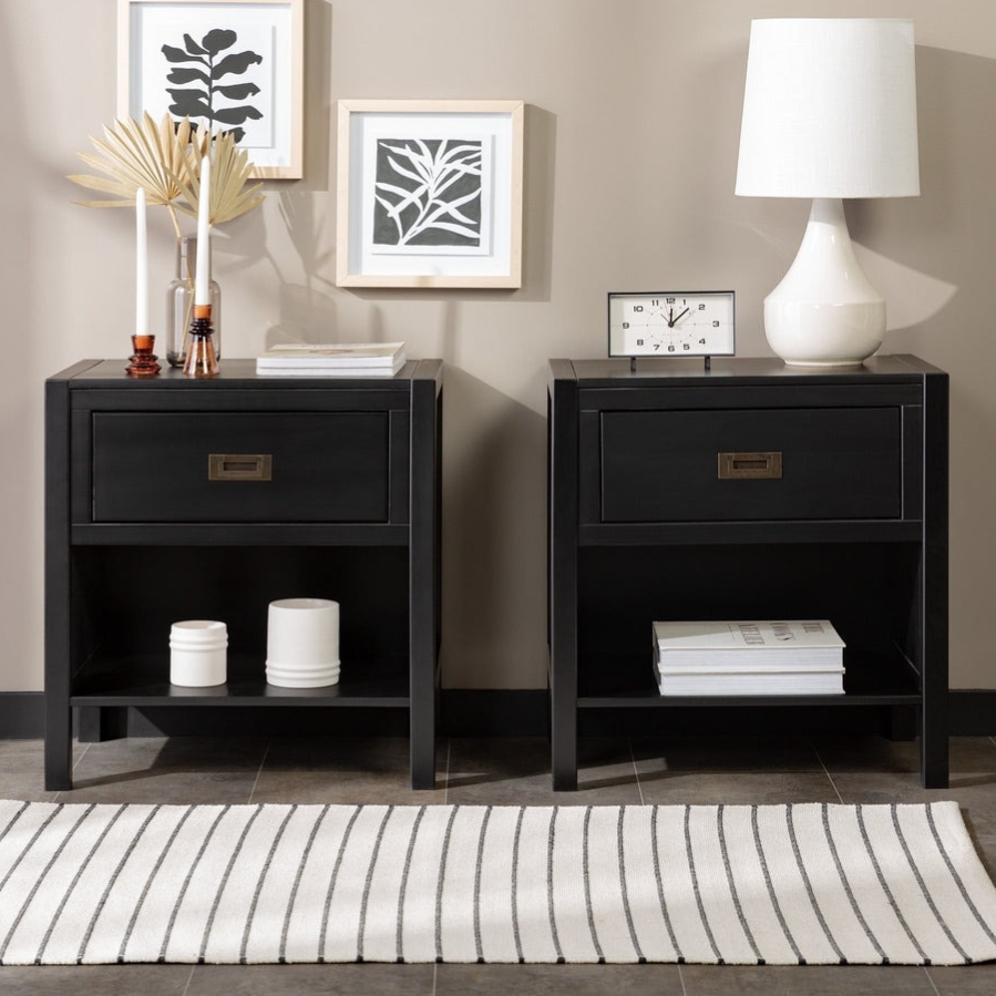 Two black nightstands with drawers; one adorned with a clock and lamp, the other with candles and decor. Wall features minimalist leaf art, and there's a striped rug on the floor.