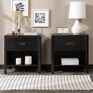 Two black nightstands with drawers; one adorned with a clock and lamp, the other with candles and decor. Wall features minimalist leaf art, and there's a striped rug on the floor.