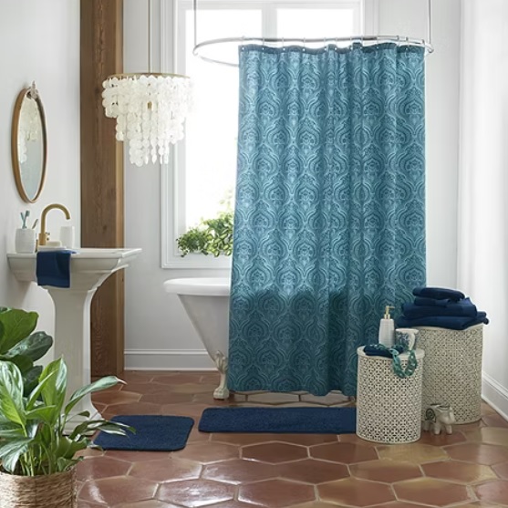 A blue patterned shower curtain, navy towels, a white chandelier, and terracotta floor tiles in a bathroom setting.