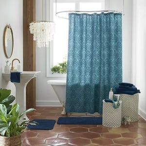 A blue patterned shower curtain, navy towels, a white chandelier, and terracotta floor tiles in a bathroom setting.