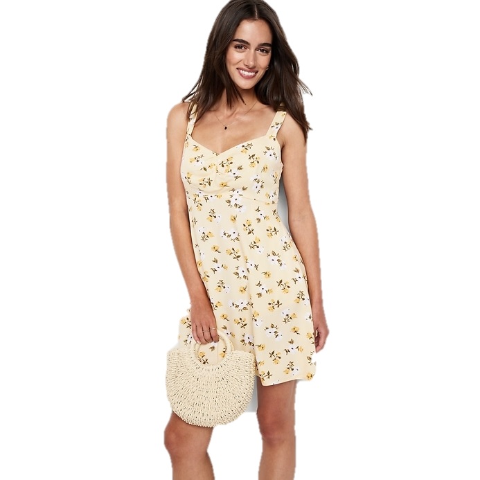 Yellow floral cami mini dress with adjustable straps, fitted bodice, and flared skirt, paired with a round straw handbag.