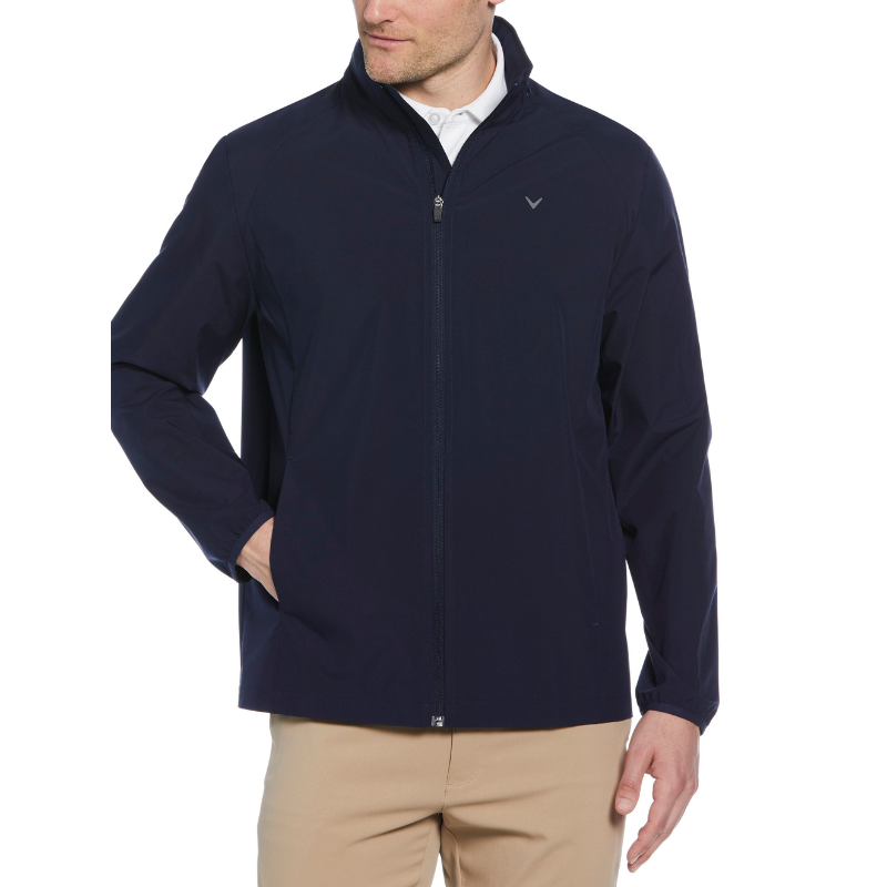 A navy blue Callaway Apparel jacket with a full zip front, featuring a small embroidered logo on the chest, is paired with beige pants. The jacket has a high collar and elastic cuffs, offering a sleek and casual look.