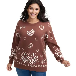 A woman is wearing a brown sweater with white paisley and floral designs, paired with blue jeans.