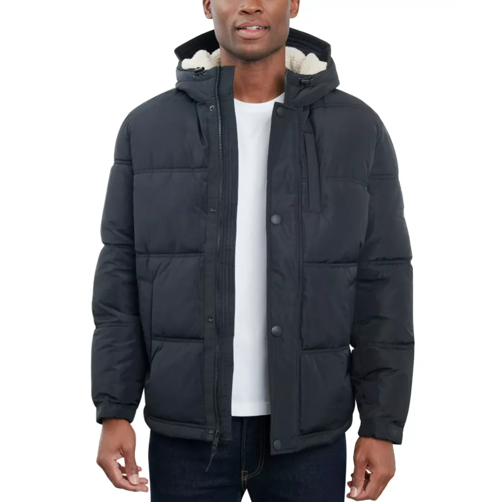 A man is wearing a black puffer jacket with a hood and sherpa lining, paired with a white t-shirt and dark jeans.