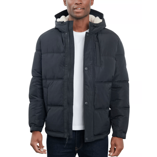 A man is wearing a black puffer jacket with a hood and sherpa lining, paired with a white t-shirt and dark jeans.