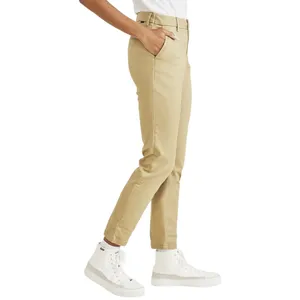 A person wearing beige slim-fit chinos, paired with white high-top sneakers and a white top, with one hand in the pocket.